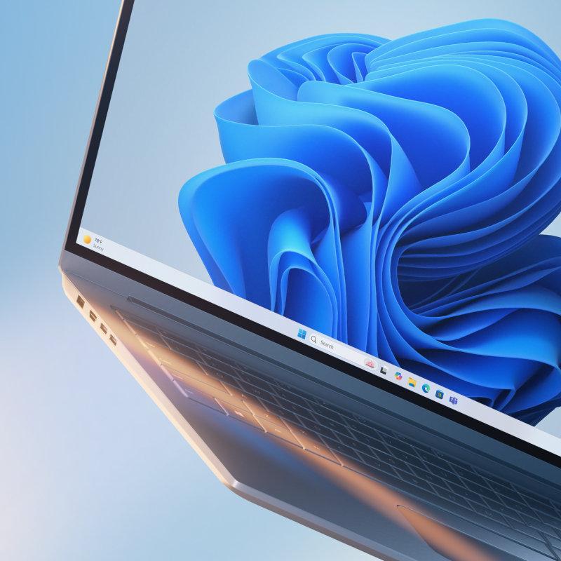 Açık mavi geçişli arka plan üzerinde mavi çiçekli ekran ile açık, eğilmiş dizüstü bilgisayarın kısmi görüntüsü.